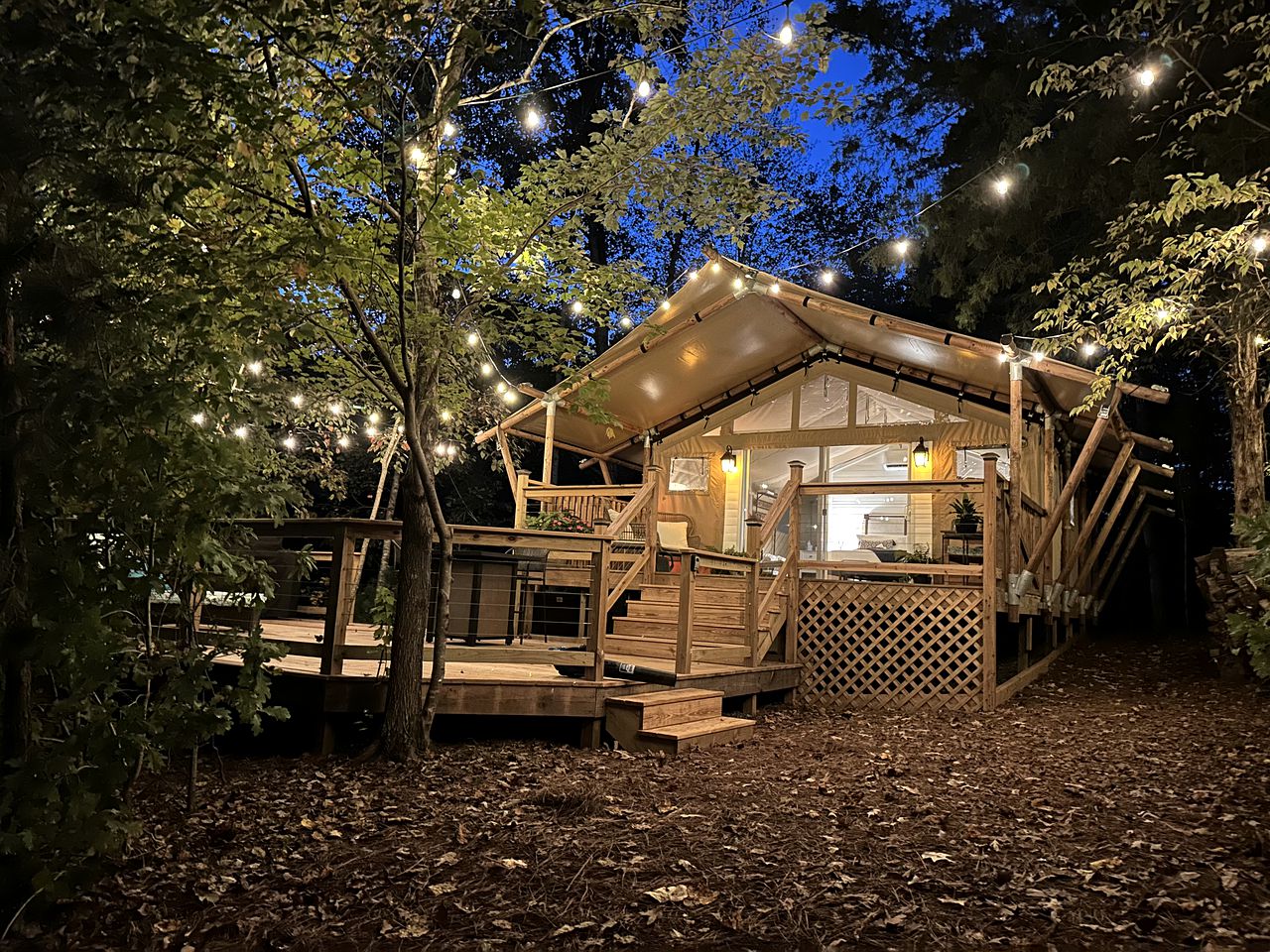 Dawson's Cove safari tent at dusk, lit by warm string lights against deep blue sky